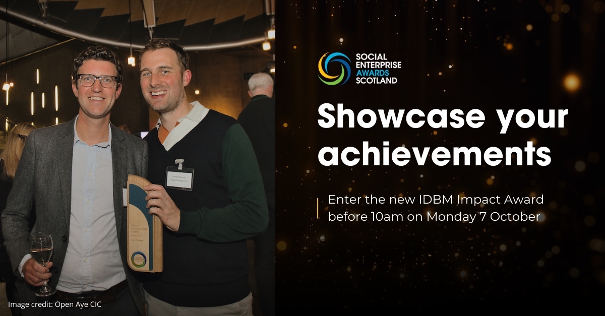 Two men are smiling at the camera and holding an award at an event. The man on the right is holding the award, and both are dressed in business casual attire.   On the right side of the image, there is a dark, glittery section with the logo for the "Social Enterprise Awards Scotland" at the top. Below the logo, the text reads:  "Showcase your achievements  Enter the new IDBM Impact Award before 10am on Monday 7 October"