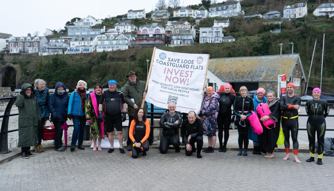 A group of people holding a banner saying 'Save Looe Coastguard Flats'