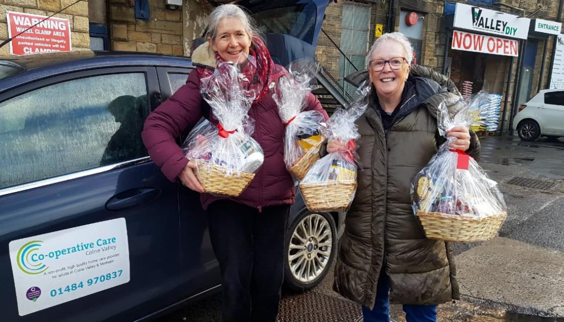 Two members of Co-operative Care Colne Valley hold Christmas hampers in front of a branded car
