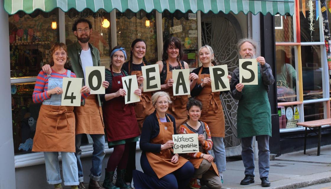 A photograph of the Trinity Wholefoods' worker-owners stood outside their Hastings shop celebrating their 40th anniversary