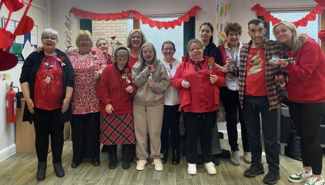 A Cartrefi Cymru group celebrates Valentine's Day: a row of people with hearts and flowers.