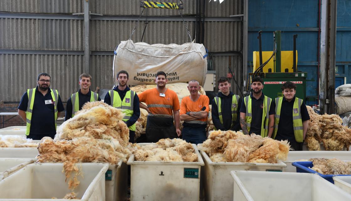 A group of workers stood smiling with wool 