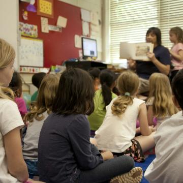 A group of children in a classroom with a teacher holding up a book