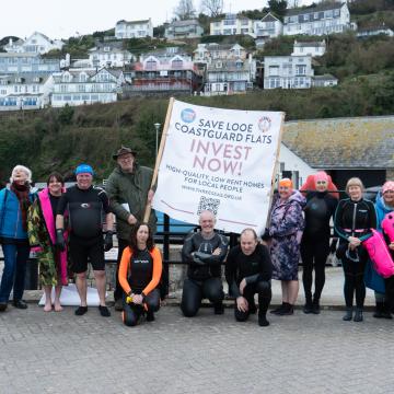 A group of people holding a banner saying 'Save Looe Coastguard Flats'