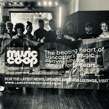 Musicians stood with a Lancaster Music Co-op banner