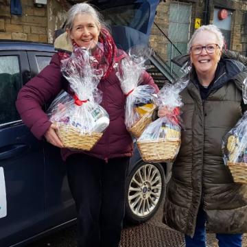 Two members of Co-operative Care Colne Valley hold Christmas hampers in front of a branded car