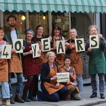 A photograph of the Trinity Wholefoods' worker-owners stood outside their Hastings shop celebrating their 40th anniversary