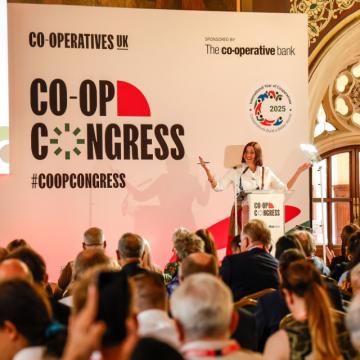 A photograph of Rose Marley, on stage at Co-op Congress 2025, addressing a packed out Rochdale Town Hall.