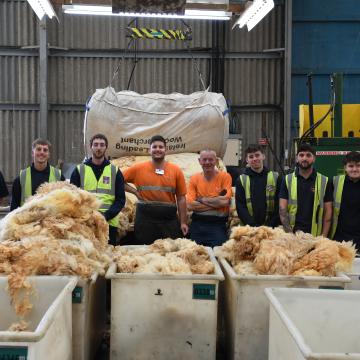 A group of workers stood smiling with wool 
